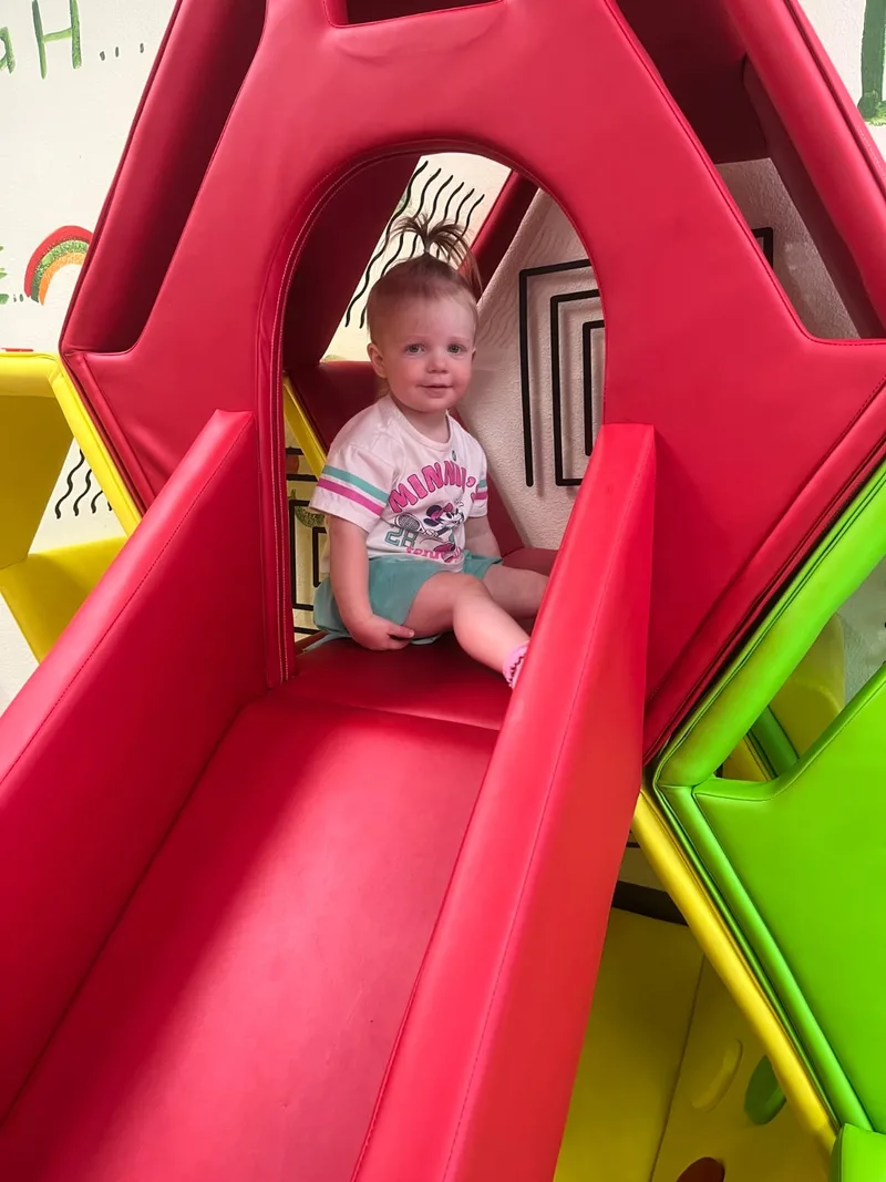 A young child enjoying a red slide at Fresh Play Cafe